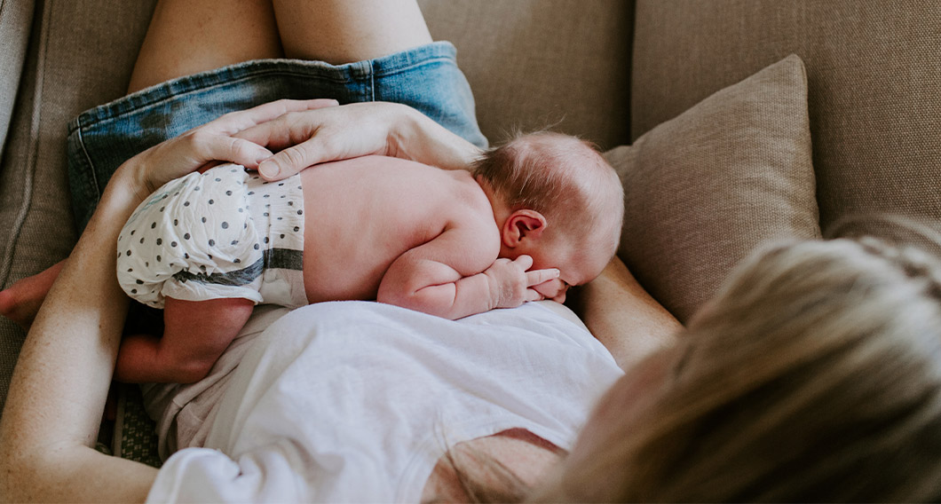 mother sitting on couch holding baby, shot from above