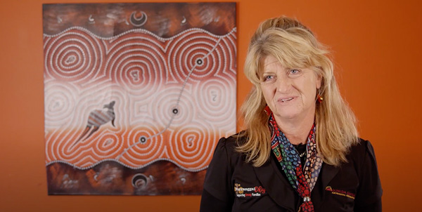 Warranggal Dhiyan staff member in front of a wall with an Aboriginal artwork  