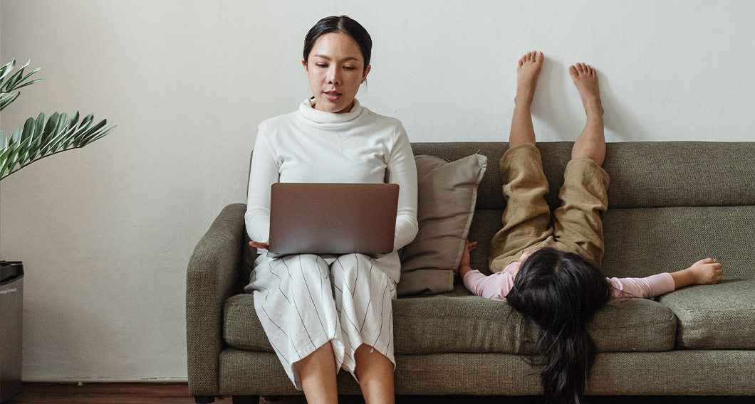 Woman working from home on the couch with a playful child beside her